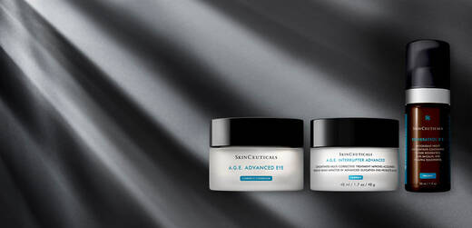 A collection of Skinceuticals skincare products displayed on a sleek, textured surface, featuring two jars labeled "A.G.E. Advanced Eye" and "A.G.E. Interrupter Advanced," along with a small serum bottle. Soft light illuminates the scene, creating a sophisticated ambiance.