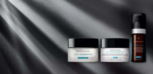 A collection of Skinceuticals skincare products displayed on a sleek, textured surface, featuring two jars labeled "A.G.E. Advanced Eye" and "A.G.E. Interrupter Advanced," along with a small serum bottle. Soft light illuminates the scene, creating a sophisticated ambiance.