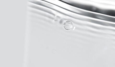 A close-up of silver water with gentle ripples and bubbles, set against a light gray background.