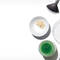 A flat lay of various makeup tools and products, including brushes, a small bowl of powder, a jar of green substance, and a mixing dish, all set against a white background.