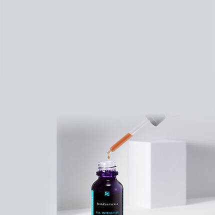 A dropper dispensing a serum from a dark glass bottle labeled "SkinCeuticals H.A. Intensifier" against a minimalistic gray background.