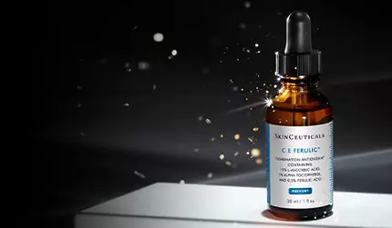 A dropper bottle of skincare serum with a dark background and soft lighting, featuring particles that create a glowing effect around it.