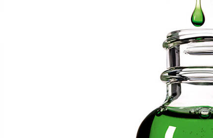 A close-up of a green liquid bottle with a drop of liquid about to fall from the neck of the bottle, set against a gradient background.