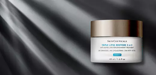 A jar of SkinCeuticals Triple Lipid Restore 2:4:2 anti-aging cream on a dark, textured background with subtle rays of light.