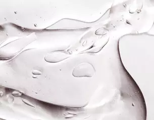 Close-up of smooth gel texture with light reflections and water droplets on a metallic surface.
