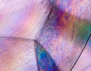 Close-up of iridescent, translucent surface displaying swirling patterns and soft pastel colours.