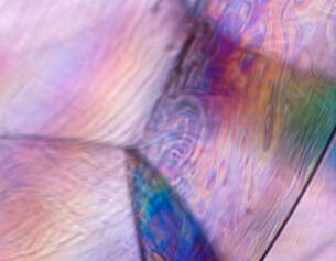 Close-up of iridescent, translucent surface displaying swirling patterns and soft pastel colours.