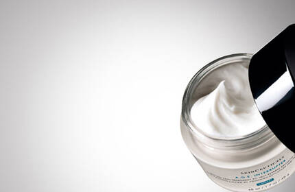 A close-up of an open jar of skincare cream against a gradient background, showcasing the creamy texture inside.