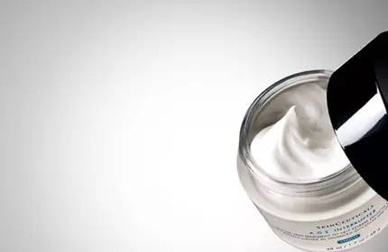 A close-up of an open jar of skincare cream against a gradient background, showcasing the creamy texture inside.