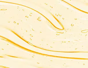 A close-up of a smooth, glossy yellow liquid with small bubbles and gentle, flowing waves in its texture.