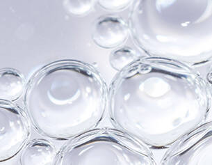 Close-up of translucent bubbles with reflections, creating a textured, shimmering surface on a light background.