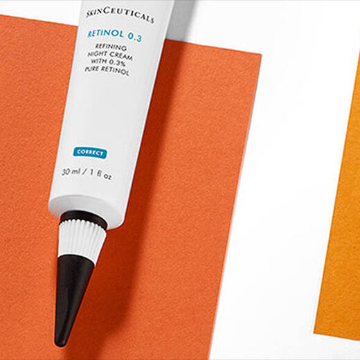 Two tubes of skincare products are positioned on a background of orange and white paper. One tube is labeled "Retinol 0.3" and features a black tip, while the other, smaller tube also displays the brand name "Skinceuticals."