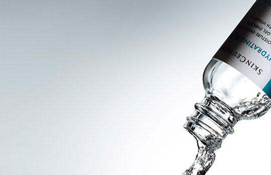 A water bottle is tilted, pouring clear water against a soft gray background.