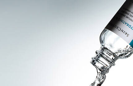 A water bottle is tilted, pouring clear water against a soft gray background.