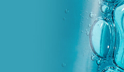 Close-up of a transparent bottle partially filled with blue liquid and bubbles, set against a light background.