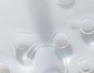 Close-up of clear liquid with various sizes of bubbles reflecting light, creating a textured and glossy surface.