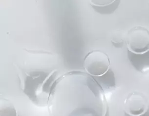 Close-up of clear liquid with various sizes of bubbles reflecting light, creating a textured and glossy surface.