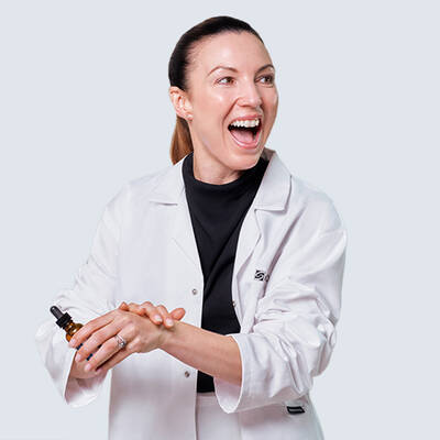 Dr. Emma Craythorne smiling whilst holding a SkinCeuticals antioxidant serum and pressing the formulation into the back of her hand