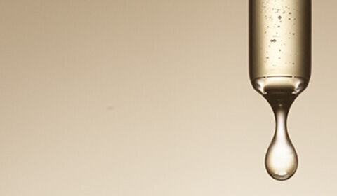 Three glass droppers, each containing a clear liquid, hang against a soft beige background, dripping at varying intervals.