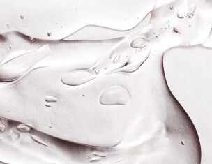 Close-up of translucent gel with droplets and smooth, flowing textures on a light background.