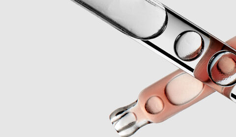 Close-up of several glass test tubes, some filled with a light pink liquid, arranged against a pale background.
