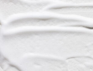 Close-up of a smooth, creamy white texture resembling whipped cream or thick lotion, with gentle grooves and swirls.