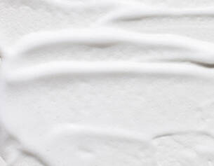 Close-up of a smooth, creamy white texture resembling whipped cream or thick lotion, with gentle grooves and swirls.