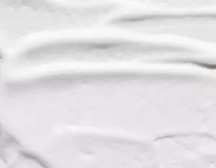 Close-up of a smooth, creamy white texture resembling whipped cream or thick lotion, with gentle grooves and swirls.