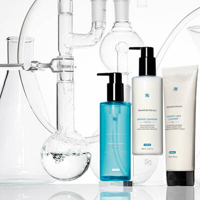 A collection of skincare products displayed in front of laboratory glassware, featuring bottles of cleanser and moisturizer with a clean and modern aesthetic.