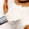 A close-up of a person's face with a white facial mask being applied using a spatula. The eye is partially visible, and the background is plain and neutral-colored.