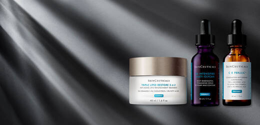 Alt text: Three skincare products from SkinCeuticals, including a jar of Triple Lipid Restore 2:4:2, and two dropper bottles labeled Vitamin C and Ferulic, set against a dramatic gray background with light rays.