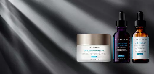 Alt text: Three skincare products from SkinCeuticals, including a jar of Triple Lipid Restore 2:4:2, and two dropper bottles labeled Vitamin C and Ferulic, set against a dramatic gray background with light rays.