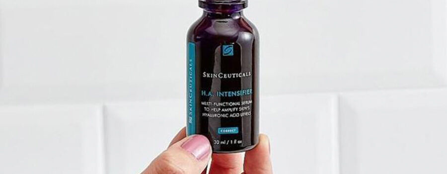 A person holding a bottle of SkinCeuticals H.A. Intensifier serum against a light background.