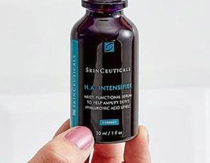 A person holding a bottle of SkinCeuticals H.A. Intensifier serum against a light background.