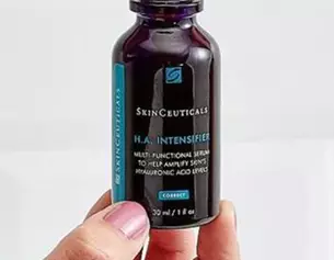 A person holding a bottle of SkinCeuticals H.A. Intensifier serum against a light background.