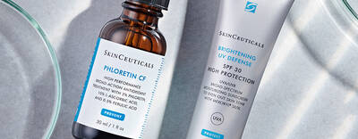 A close-up of two SkinCeuticals products: a brown glass bottle labeled "Phloretin CF" and a tube labeled "Brightening UV Defense SPF 30." The products are placed on a light surface, surrounded by small glass dishes.