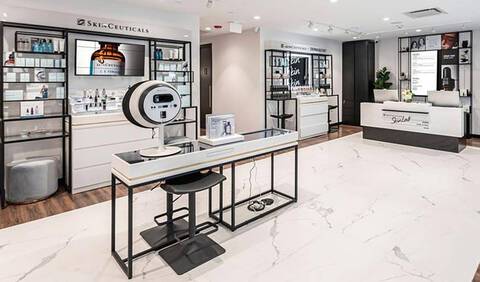A modern retail space featuring sleek display shelves and a central white countertop with minimalist furniture. The atmosphere is bright and inviting, showcasing skincare or beauty products.