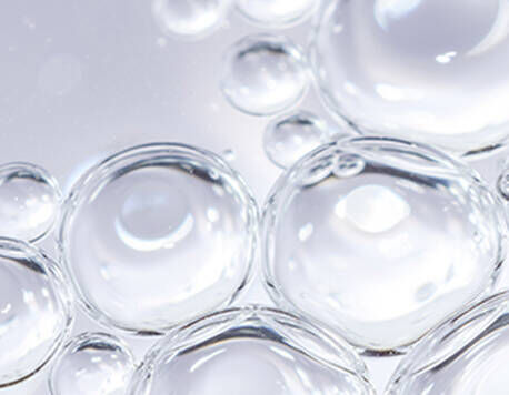 Close-up of clear water droplets, showcasing their spherical shapes and reflections against a light background.