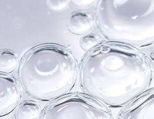 Close-up of clear water droplets, showcasing their spherical shapes and reflections against a light background.