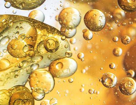 Close-up of golden oil bubbles suspended in a bright liquid, creating an abstract and shimmering effect.