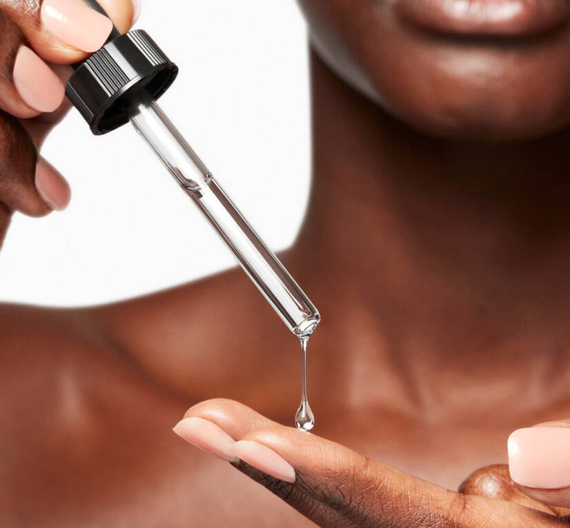 A person holding a dropper bottle, releasing a clear serum onto their palm, with a focus on skincare.