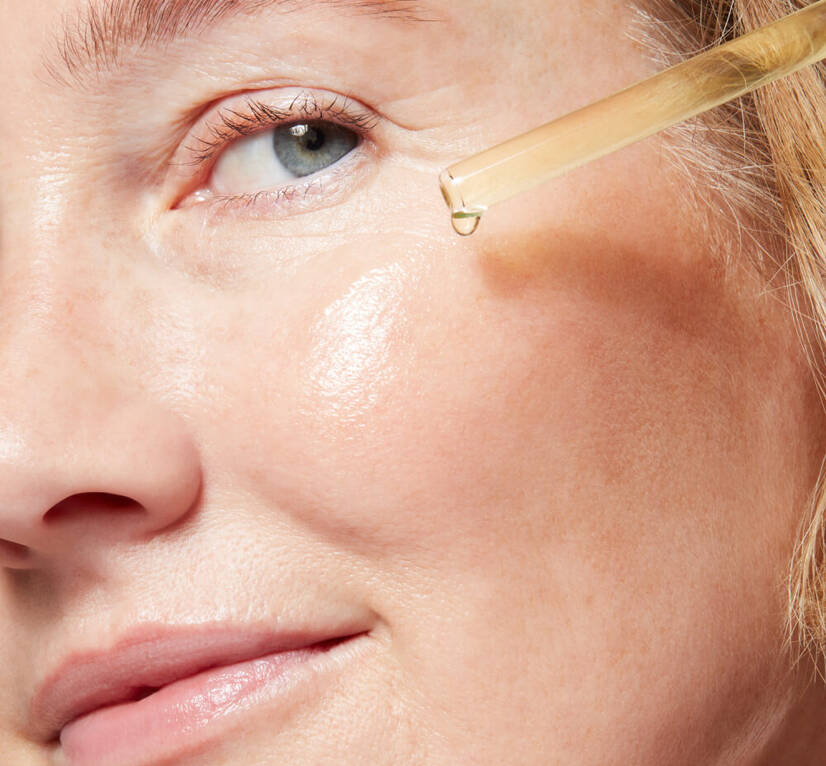 Close up of woman’s face, holding a pipette of C E Ferulic serum to her cheek