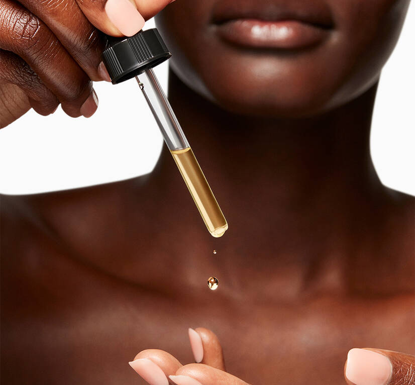 Woman dispensing a golden liquid from a pipette onto her fingertips