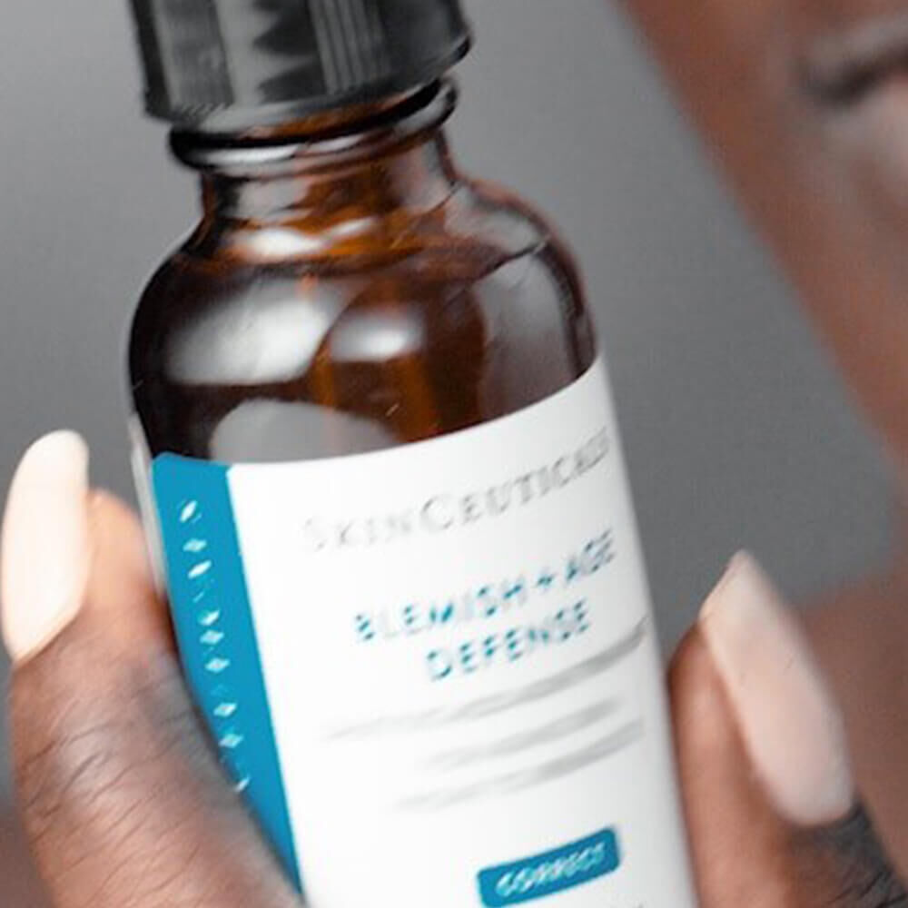 A close-up of a hand holding a brown bottle of SkinCeuticals Blemish + Age Defence serum.