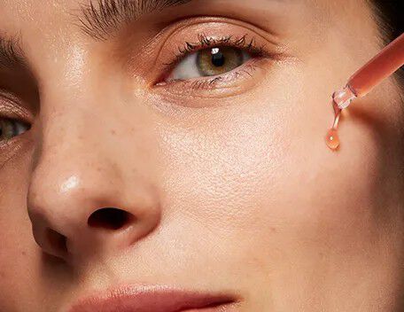Woman lifting a pipette with a pink serum to her cheek