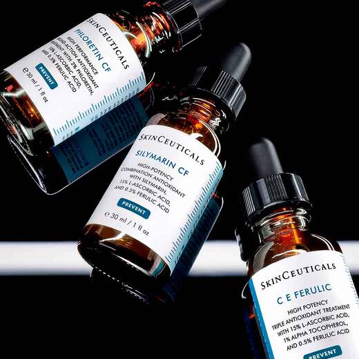 n amber glass bottle of SkinCeuticals Silymarin CF, between two other similar bottles C E Ferulic and Phloretin CF, against a dark background