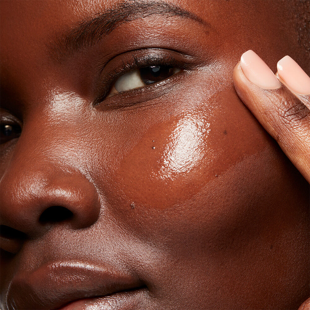 Close up of a woman swiping a clear serum onto her cheek, creating a radient glow
