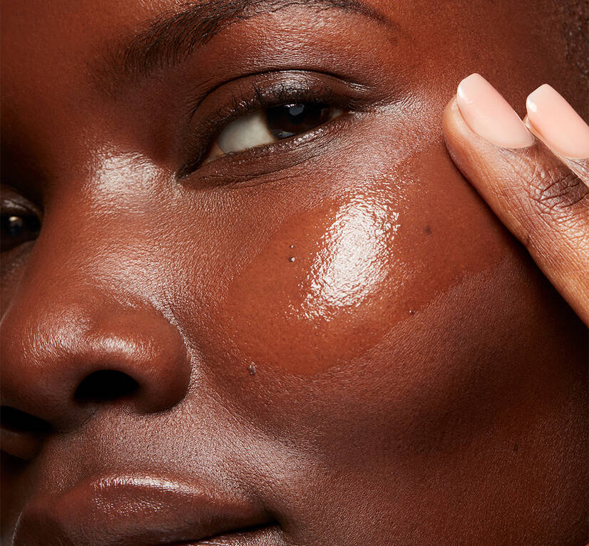 Close up of a woman swiping a clear serum onto her cheek, creating a radient glow