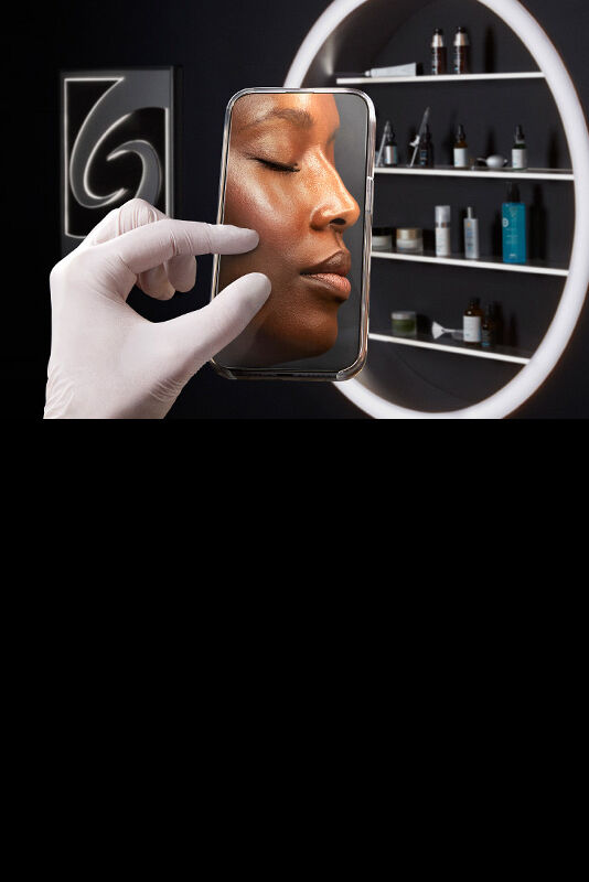 A hand in a white glove holds a smartphone displaying a close-up of a woman's face with glowing skin, set against a backdrop of shelves featuring various skincare products.