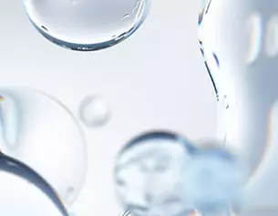 Close-up of shimmering water droplets against a light background, showcasing clarity and reflection.